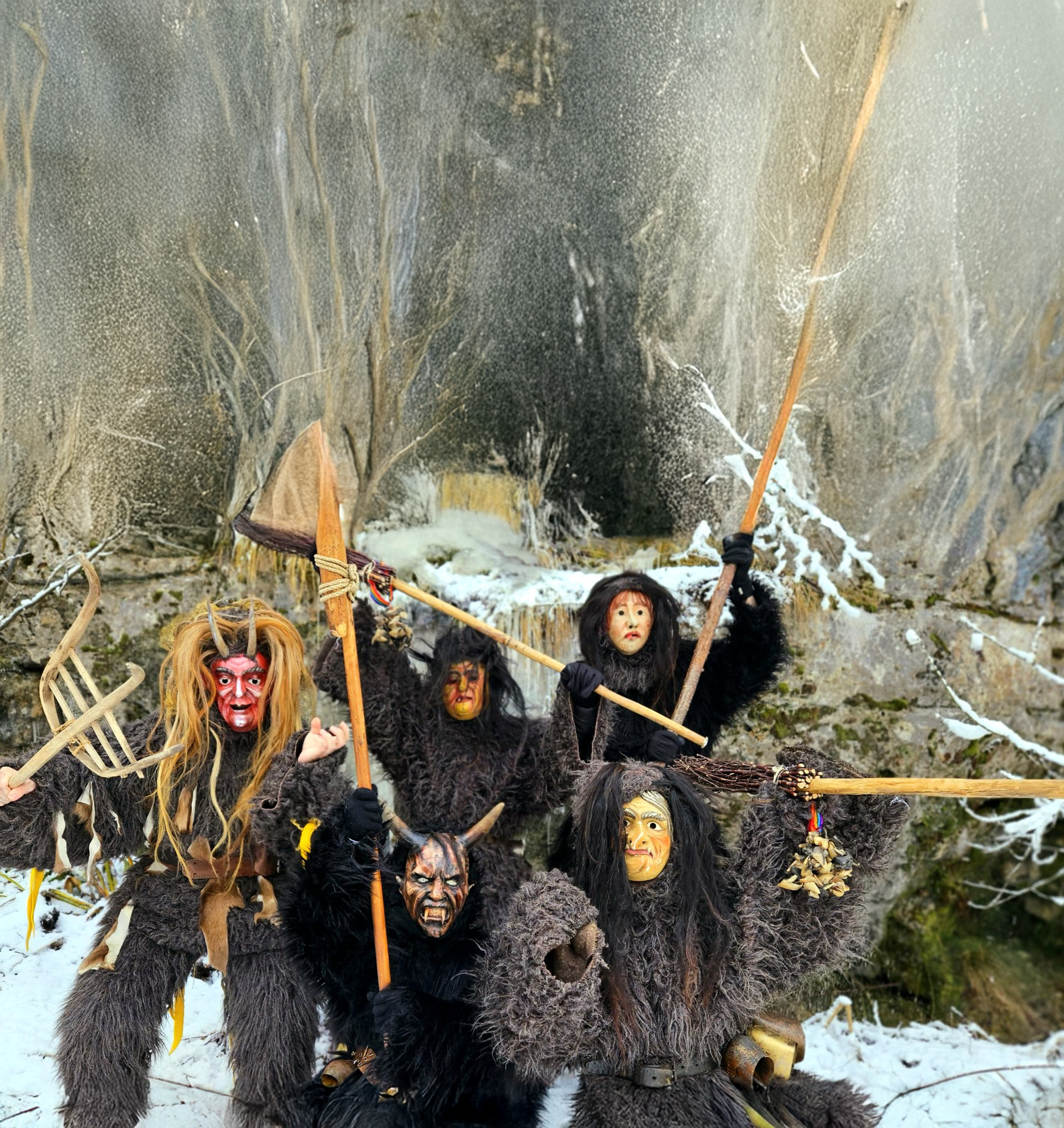 Gruppe traditioneller Perchten in Fellkostümen und Holzmasken im winterlichen Alpenraum, Darstellung des Perchtenlaufs.