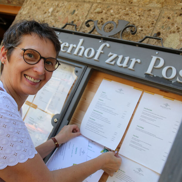 Viktoria Brummer befestigt lächelnd die neue Frühjahrs- und Sommer-Speisekarte im Schaukasten am Eingang des Klosterhofs zur Post in Bayrischzell.