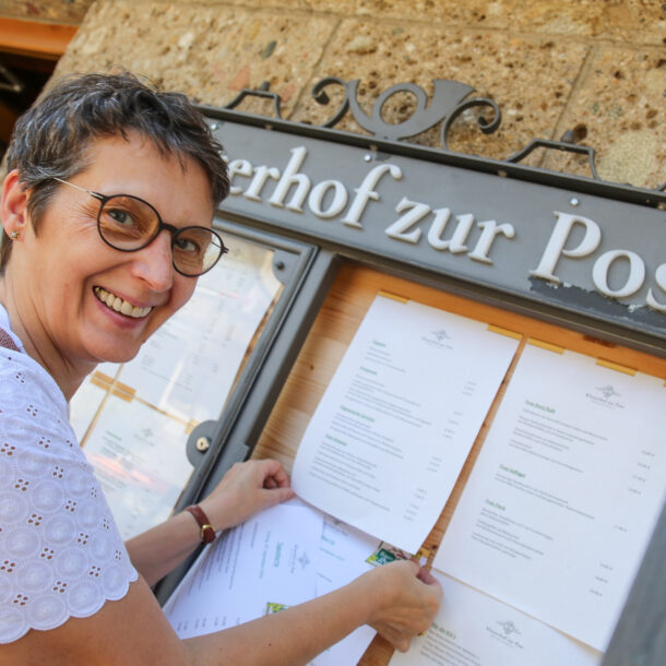 Viktoria Brummer befestigt lächelnd die neue Frühjahrs- und Sommer-Speisekarte im Schaukasten am Eingang des Klosterhofs zur Post in Bayrischzell.