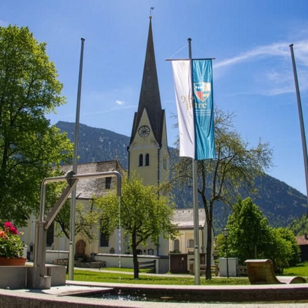 Pfarrkirche St. Margareth in Bayrischzell mit Jubiläumsfahne vor Bergkulisse und blauem Himmel – aufgenommen im Rahmen des Jubiläums 950 Jahre Bayrischzell und Kloster Scheyern.